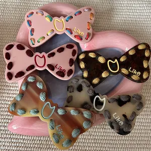 Colorful Y2K style bow-shaped hair clips with hand-embroidered edges on a pink tray