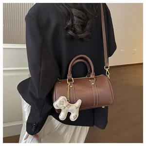 Elegant brown Boston pillow bag with cute puppy charm worn on a model's shoulder.