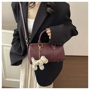 Detailed view of burgundy leather Boston bag with decorative monogram dog charm.