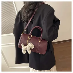 Detailed view of an elegant burgundy Boston bag with cute puppy charm on black blazer.