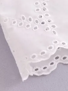Macro detail of white cotton shirt with intricate eyelet embroidery and scalloped edges.