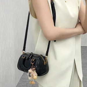 Model wearing a black mini Boston crossbody bag with a fuzzy doll keychain attached.
