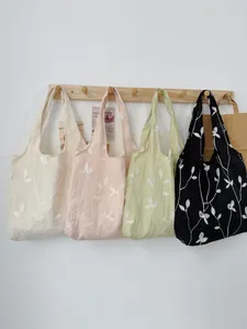 Multiple colors of embroidered butterfly canvas tote bags hanging on a wooden rack