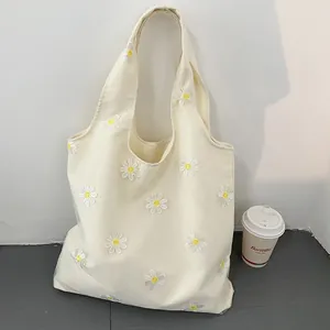 Detailed view of a stylish cream canvas tote bag featuring embroidered white daisy patterns