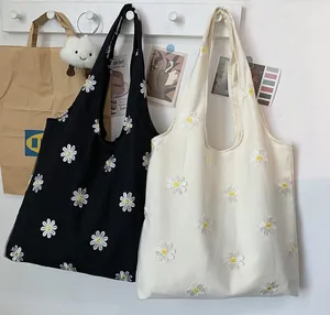 Detailed display of black and white canvas tote bags with delicate daisy embroidery pattern.