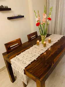 Hand-woven macrame table runner with fringe on a dark wooden dining table.