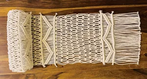 Detailed texture of bohemian handmade macrame table runner with fringes on wood table.