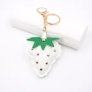 Detail view of a white leather strawberry keychain with gold studs and metal ring