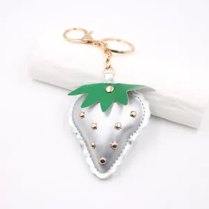 Close-up of a silver metallic leather strawberry keychain with gold studs and hardware