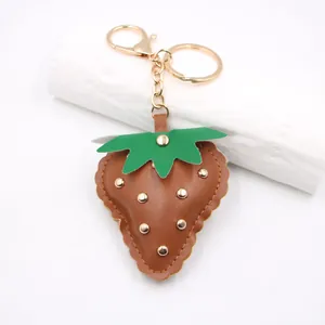 Detail view of brown leather strawberry keychain with gold studs and lobster clasp.