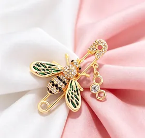 Elegant gold-toned bee brooch with green enamel wings and crystals on soft pink silk.