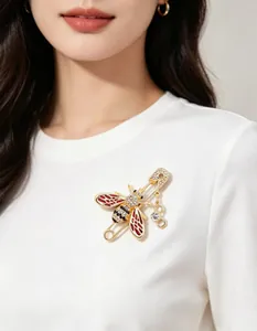 Detail shot of a gold-tone bee brooch with red enamel and rhinestones on a white shirt.