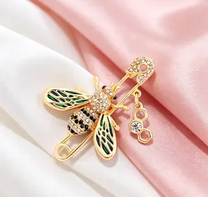 Macro view of gold-tone bee brooch with green enamel wings and crystal details