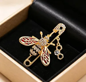 Close-up of gold-finish bee brooch with rhinestones and red enamel wings in a gift box