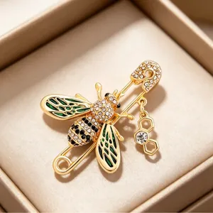 Elegant gold bee brooch with green enamel and crystals on a decorative safety pin.
