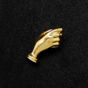 Detailaufnahme einer goldfarbenen Brosche in Handform auf schwarzem Stoffgrund.