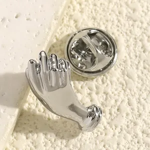 Detailansicht einer polierten silberfarbenen Brosche in Handform mit einem Schmetterlingsverschluss.