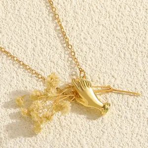 Detailed close-up view of a creative gold hand pendant necklace with dried flowers.