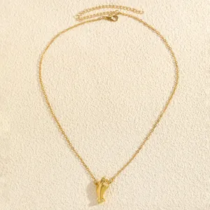 Detailed view of a gold-plated hand pendant necklace on a textured background.