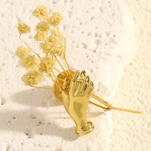 Detailed close-up of a creative gold hand-shaped brooch holding delicate yellow dried flowers.