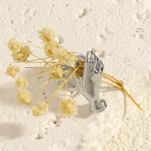 Detailed view of a silver hand-shaped brooch holding a bunch of delicate yellow dried flowers