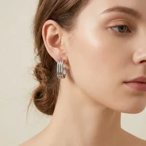 Detailed close-up of minimalist multilayered silver oval hoop earrings worn by a model.