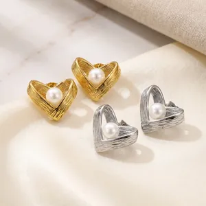 Nahaufnahme von gold- und silberfarbenen Herz-Ohrringen mit Perlen auf Seidensatin.