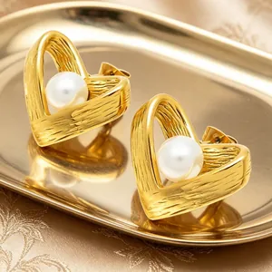 Nahaufnahme goldener Herz-Ohrstecker mit weißer Perle und edler Holzmaserung-Oberfläche