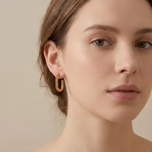 Detailed close-up of gold-plated stainless steel square twist hoop earrings on ear.