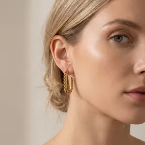Close-up detail of a minimalist gold twisted stainless steel hoop earring on a model.