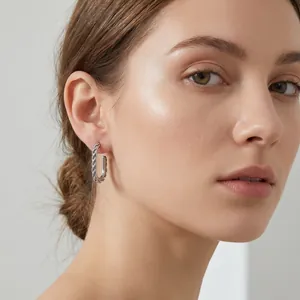 Close-up of a model wearing a twisted rectangular silver stainless steel hoop earring