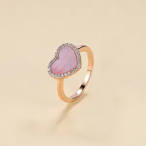 Rose gold heart ring with pink shell inlay and pavé stones on beige background.