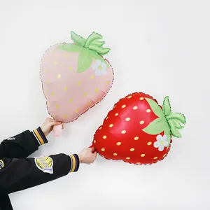Large red and pink strawberry foil balloons held by hands for birthday party decorations.