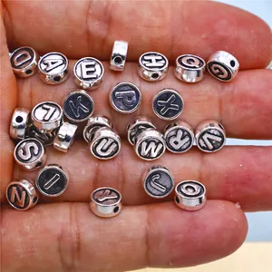 Macro view of twenty-six double-sided silver alloy alphabet charms held in a hand