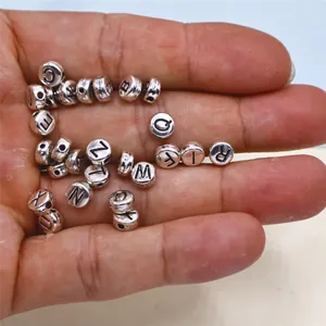 Close-up view of 26 silver alloy alphabet beads held in hand for DIY jewelry crafts