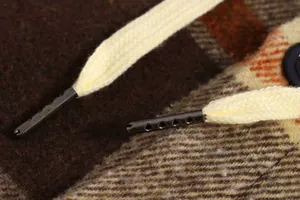 Macro detail of metal aglets on cream drawstrings of a plaid hooded shirt jacket