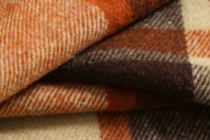 Macro detail of soft plaid flannel shirt fabric texture in orange and brown earthy tones.
