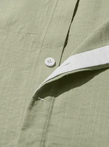 Macro detail of a sage green textured linen shirt button placket with a white button.