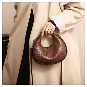Close-up of a stylish brown woven texture crescent shoulder bag held by a person