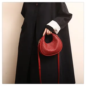 Close-up detail of a stylish red woven leather crescent handbag held by a fashion model