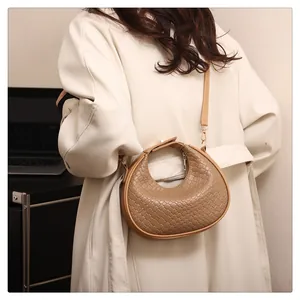 Detailed view of a khaki woven hobo crescent bag worn with a stylish beige trench coat