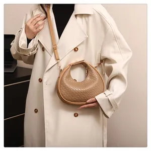 Close-up of a stylish tan woven crescent shoulder bag worn with a classic cream trench coat