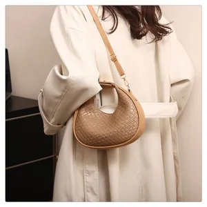 Close-up view of a chic woven beige crescent shoulder bag worn with a white coat