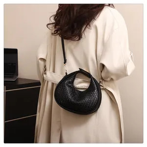 Back view of a woman wearing a black woven crescent shoulder bag over a beige coat