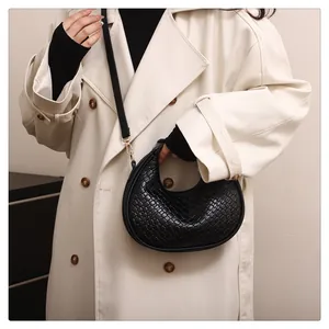Detail of a black woven crescent handbag styled with a minimalist beige trench coat.