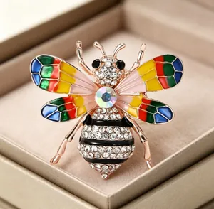 Gros plan d'une broche abeille en émail coloré avec strass dans un écrin à bijoux beige