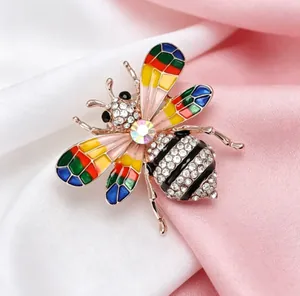 Détail d'une broche abeille en strass colorés sur un tissu de soie rose et blanc