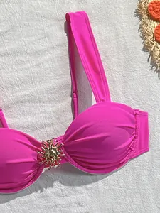 Vue rapprochée d'un haut de bikini rose vif avec décoration en métal doré en forme de soleil