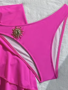 Gros plan du bas de bikini rose vif avec un charm décoratif en métal en forme de soleil doré