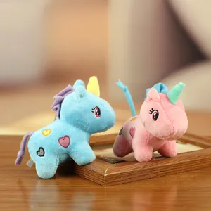 Gros plan de deux adorables porte-clés licorne en peluche rose et bleu sur un cadre bois.